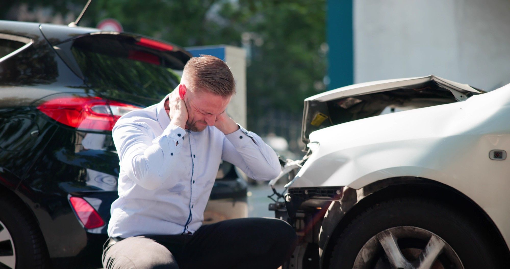 A man holding his neck in pain beside two cars after a rear-end collision.