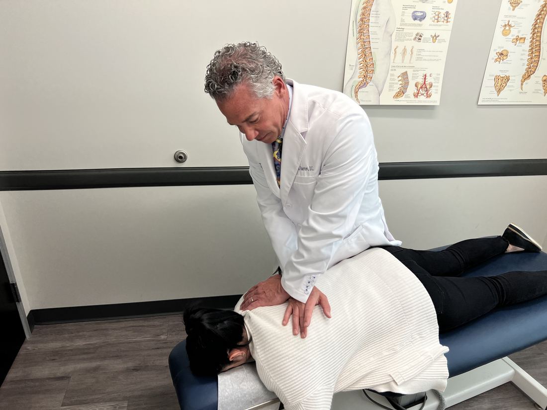 Dr. Kevin S. Barton, D.C., with both hands on the upper back of a patient lying face down on a treatment table at Texas Spine Clinic.