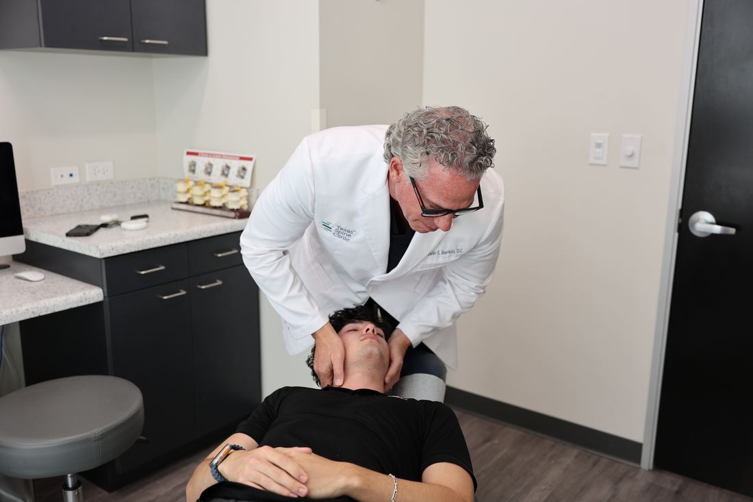 Dr. Kevin S. Barton, D.C., with his hands on the sides of a patient's neck for a neck adjustment, the patient's head resting on the table's headrest, at Texas Spine Clinic.