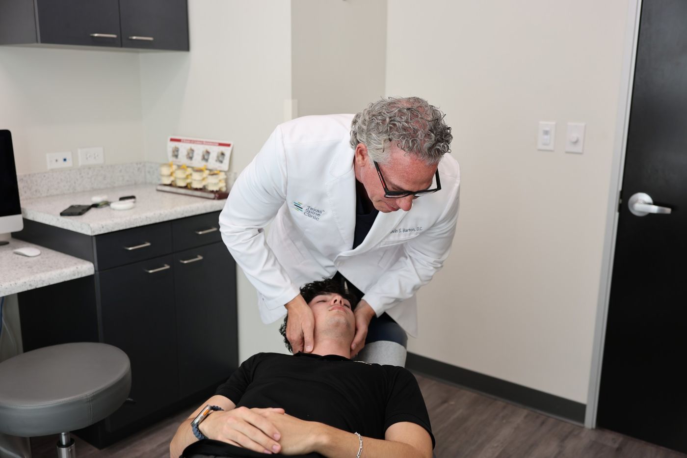 Kevin S. Barton, D.C., performing a cervical adjustment on a patient lying face up, the patient's head cradled and supported in his hands.