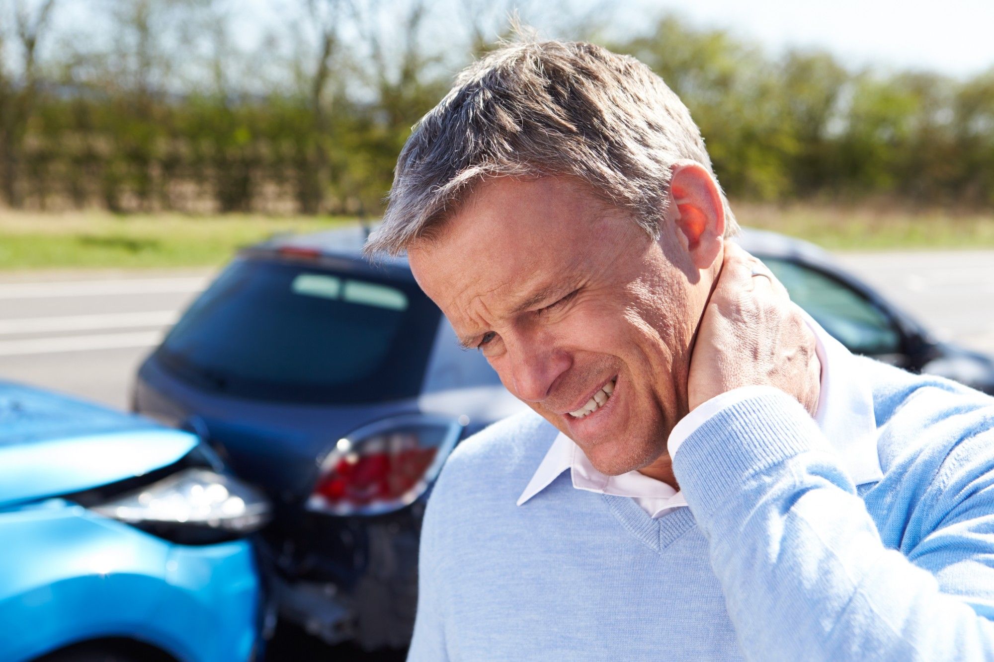 A man holding the back of his neck in pain beside two cars after a rear-end collision.