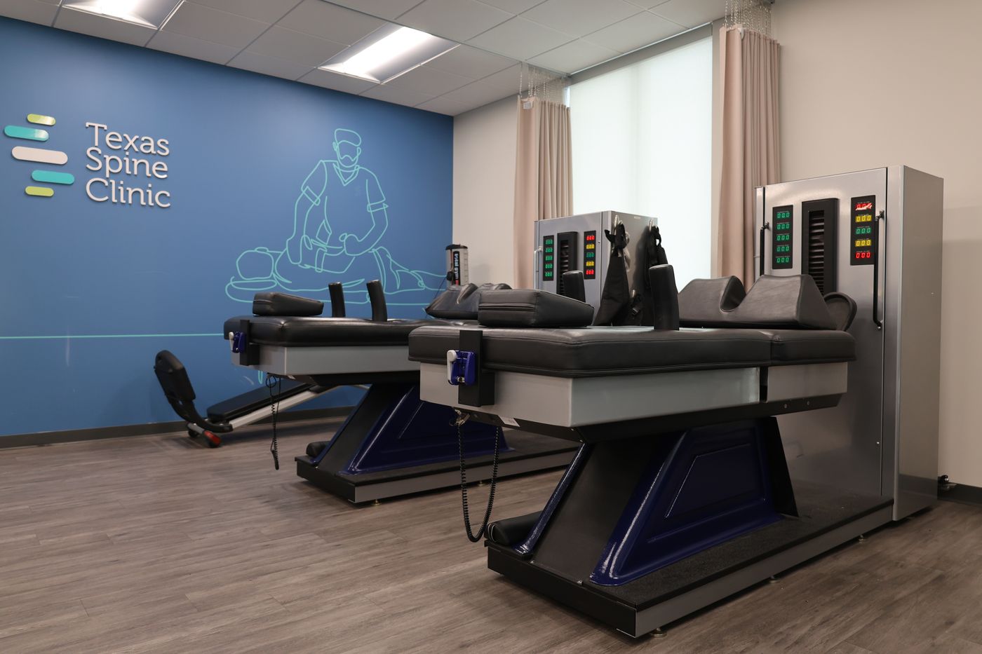 Two DRX9000 spinal decompression tables in the Texas Spine Clinic treatment room, in front of the clinic's logo wall.