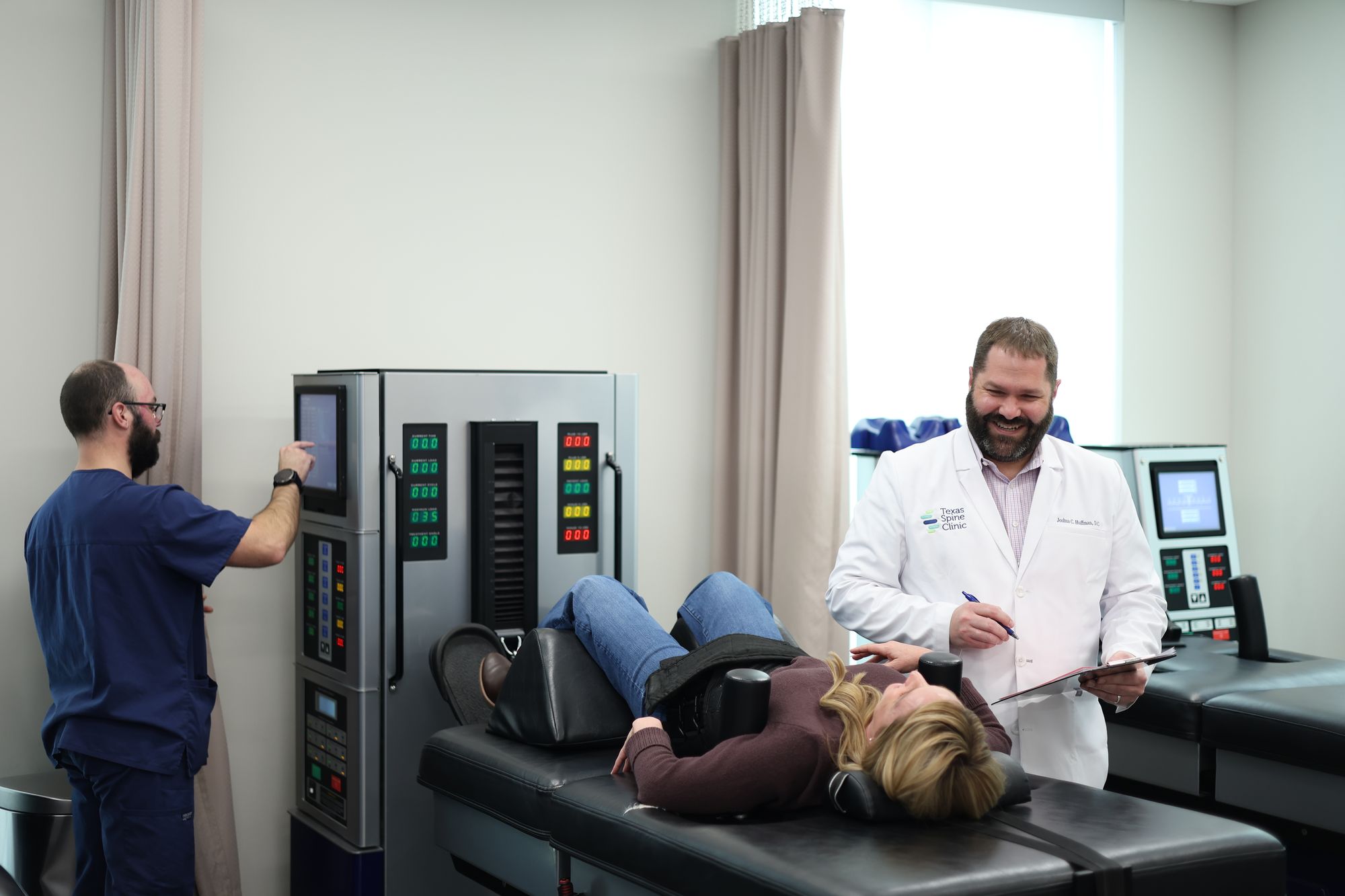 Joshua C. Huffman, D.C., charting beside a patient on the DRX9000 while a technician sets the machine.