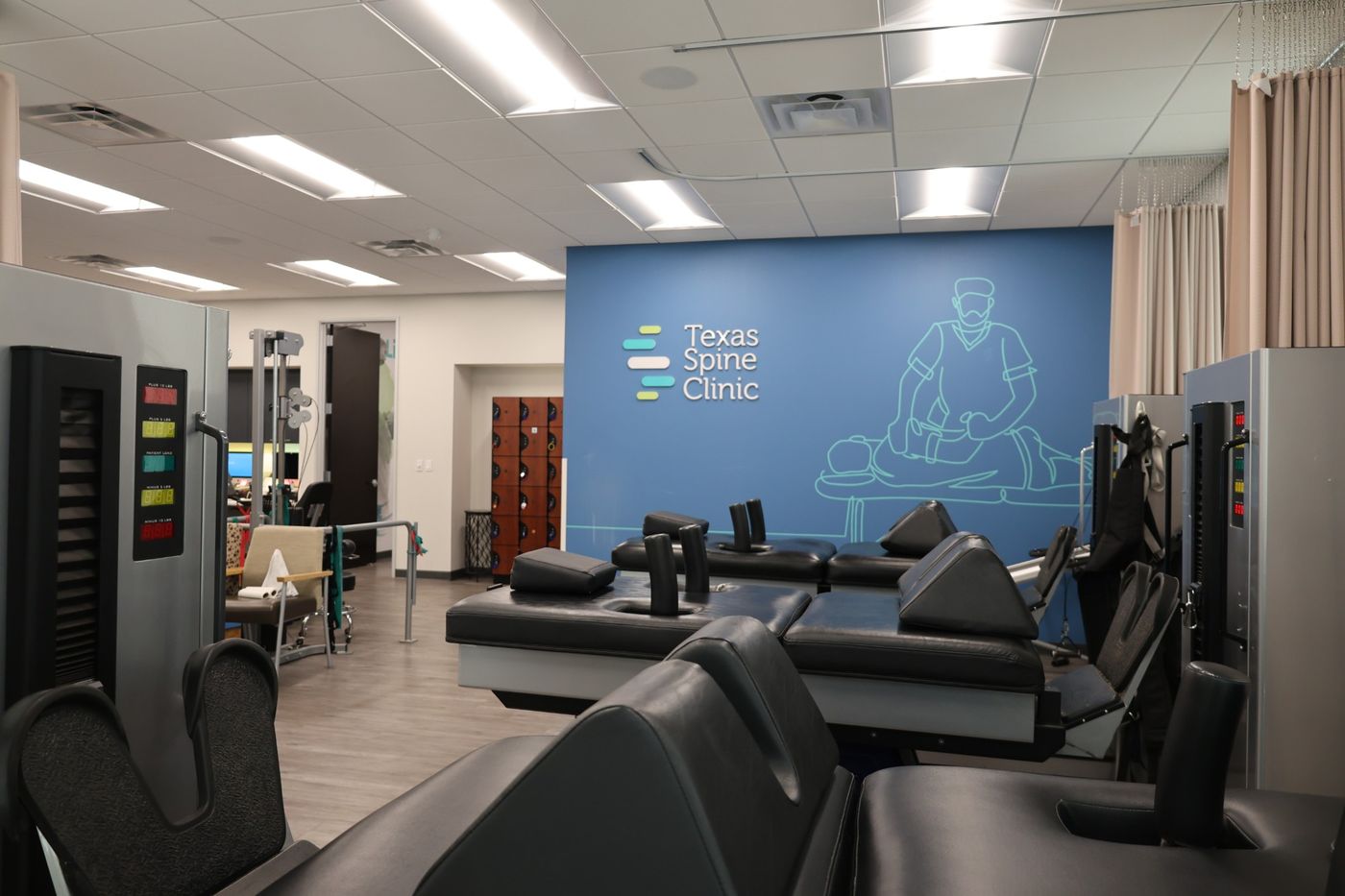 DRX9000 spinal decompression tables in the Texas Spine Clinic treatment room, in front of the clinic's logo wall.