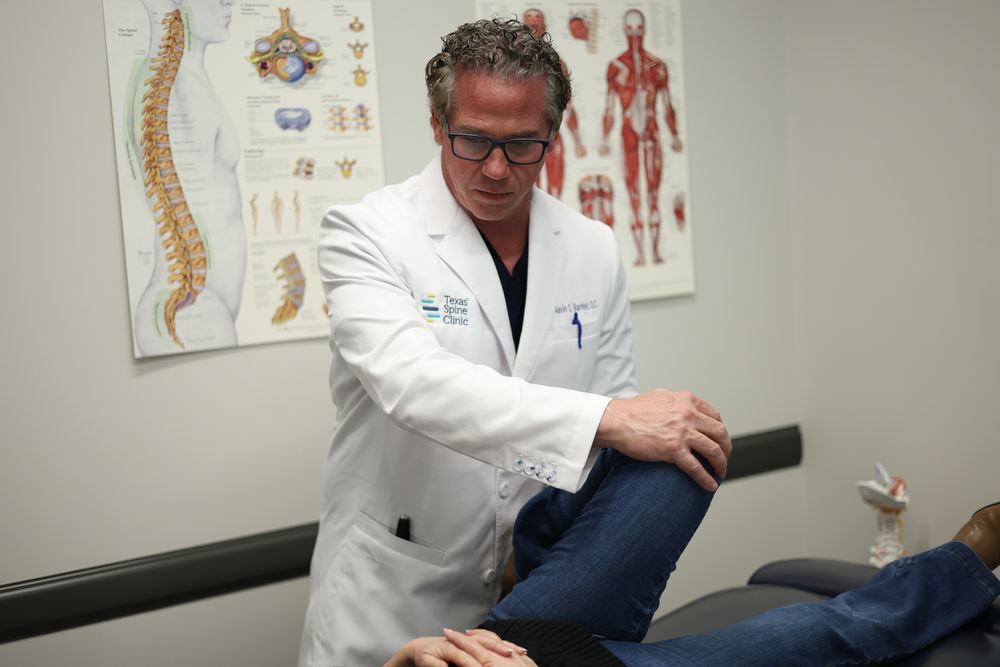 Kevin S. Barton, D.C., bending a patient's knee toward the chest during an exam to load the joints at the back of the spine.