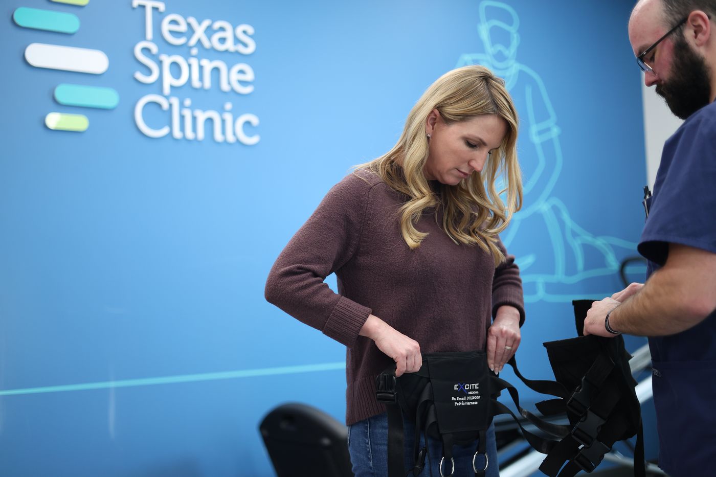 A Texas Spine Clinic team member fitting the DRX9000 pelvic harness around a patient's hips before treatment.