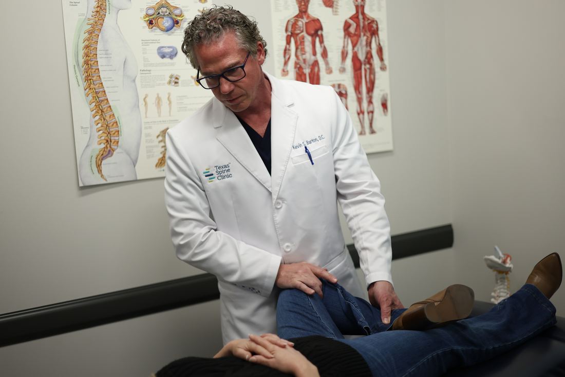 Dr. Kevin S. Barton, D.C., bending a patient's hip and knee to test how the joints move, with the patient lying on a treatment table at Texas Spine Clinic.