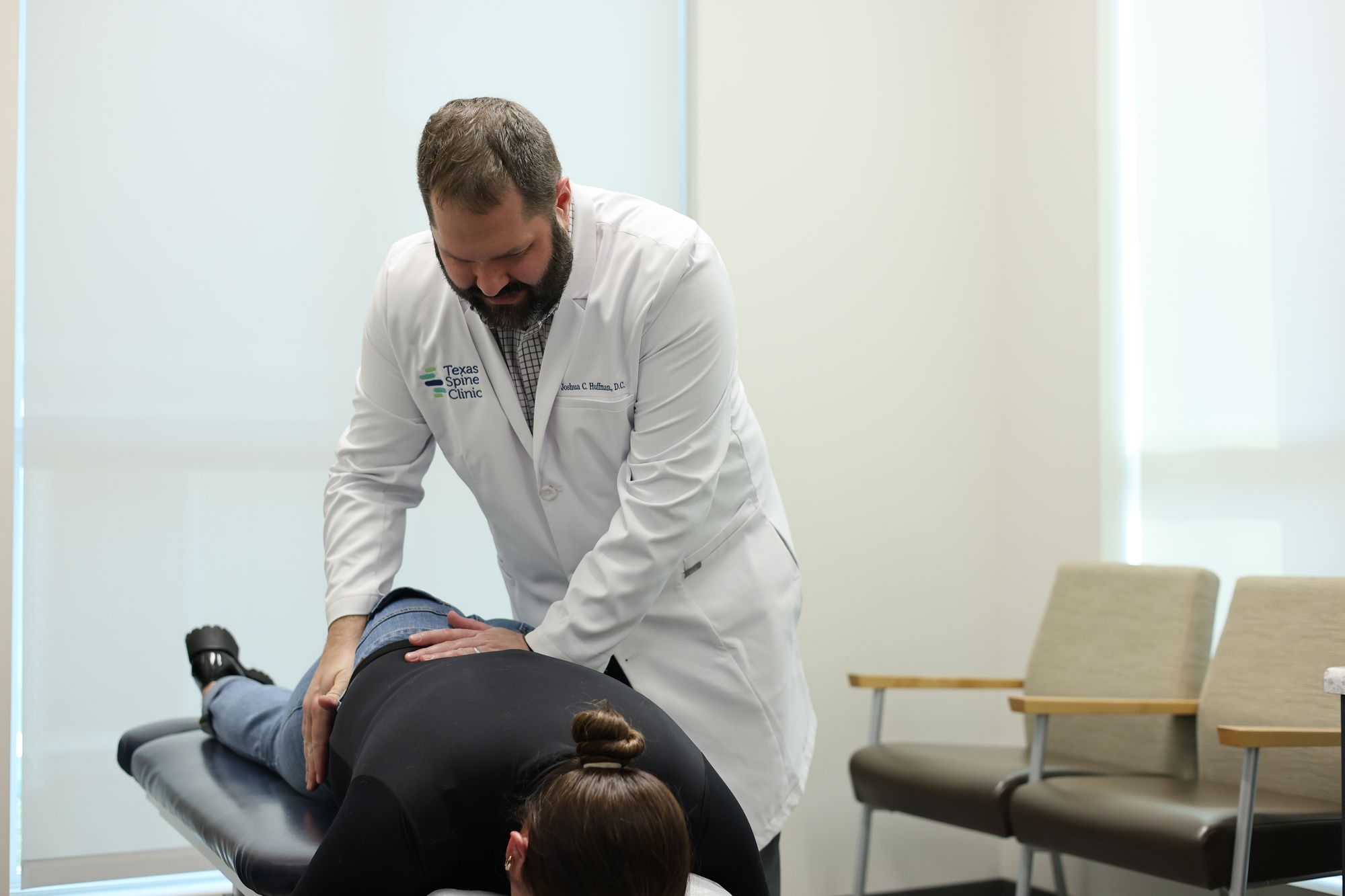 Dr. Joshua C. Huffman palpating a prone patient's lower back during a facet syndrome examination.