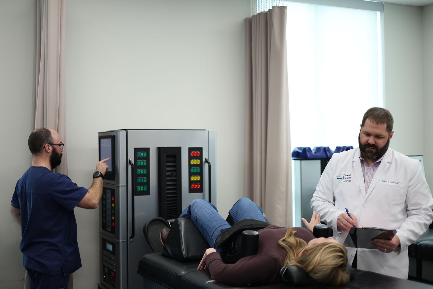 A patient lying on the DRX9000 table while a team member sets the console and Dr. Huffman reviews her chart.