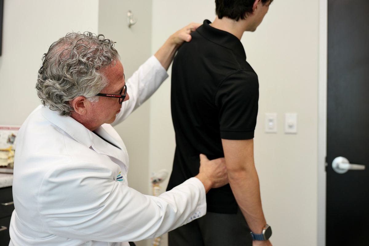 Dr. Barton checking a standing patient's posture with one hand on his shoulder and one on his lower back.