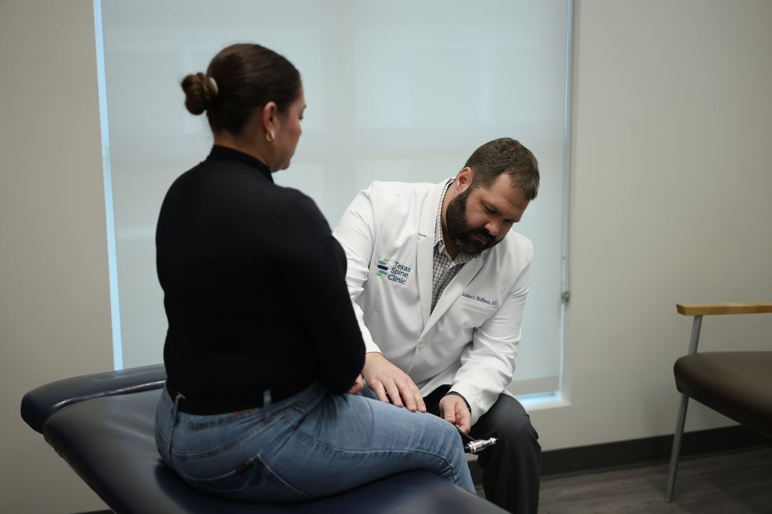 Dr. Joshua C. Huffman, D.C., testing a seated patient's knee reflexes with a reflex hammer at Texas Spine Clinic.