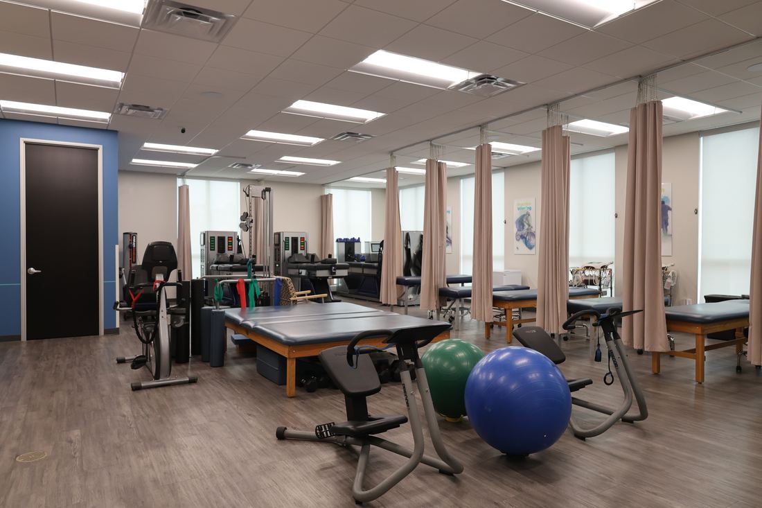 The rehabilitation room at Texas Spine Clinic: therapy tables, a stationary bike, exercise balls and training equipment.