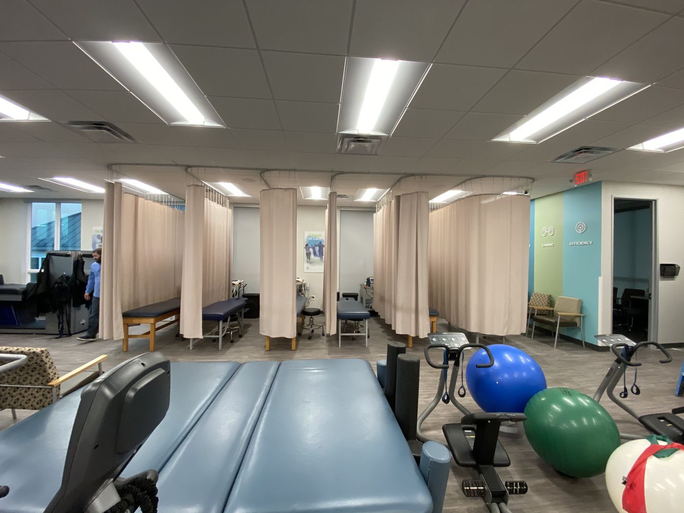 The Texas Spine Clinic rehab room seen from the other end: therapy tables, curtained treatment bays, exercise balls and bikes.