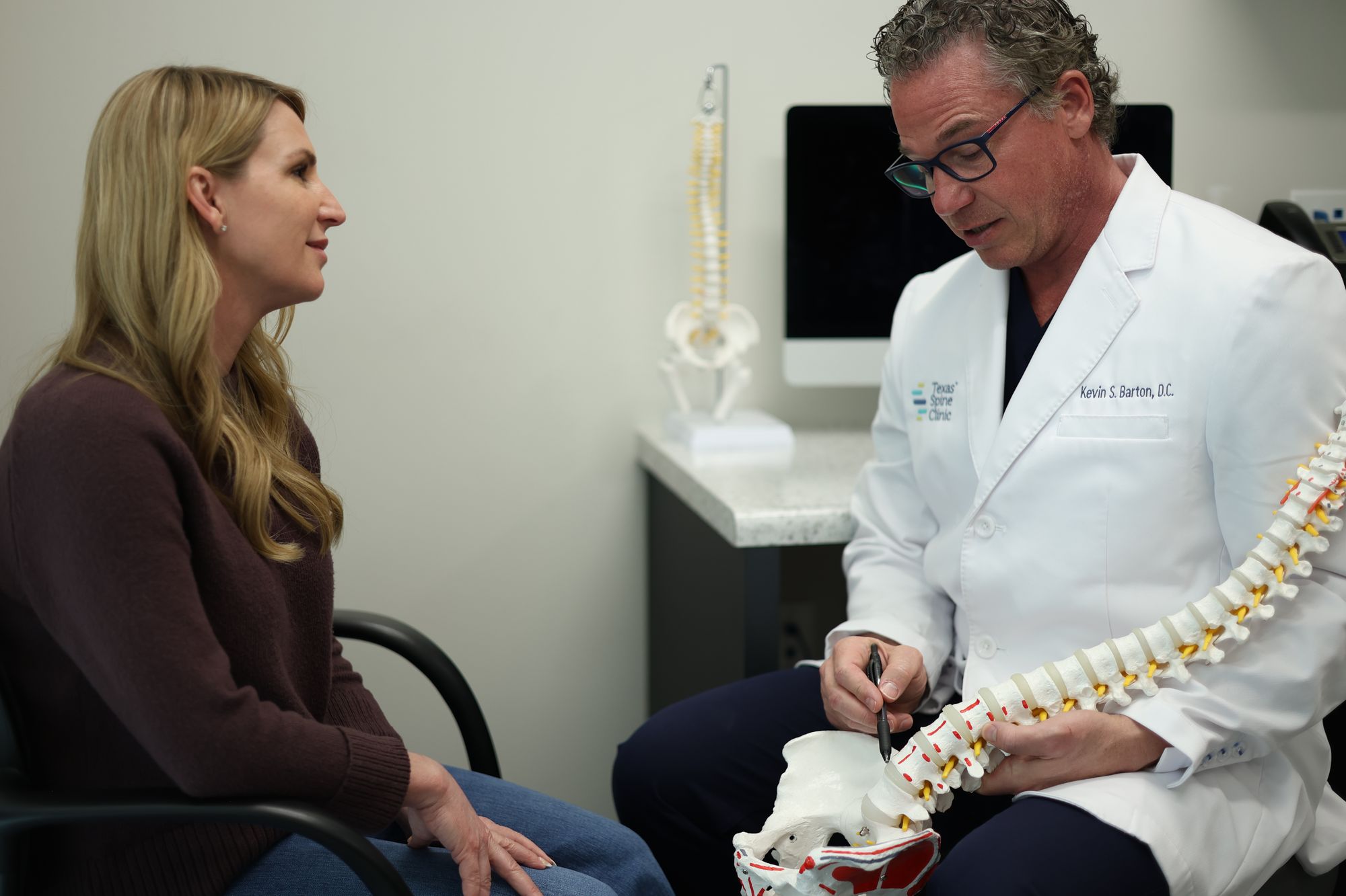 Dr. Kevin Barton using a model of the spine to explain a disc bulge to a patient seated across from him.