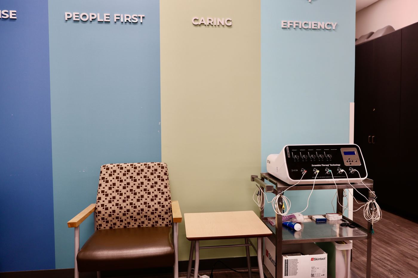 The scrambler treatment chair beside the cart holding the ST-5A machine, in front of the clinic's values wall.