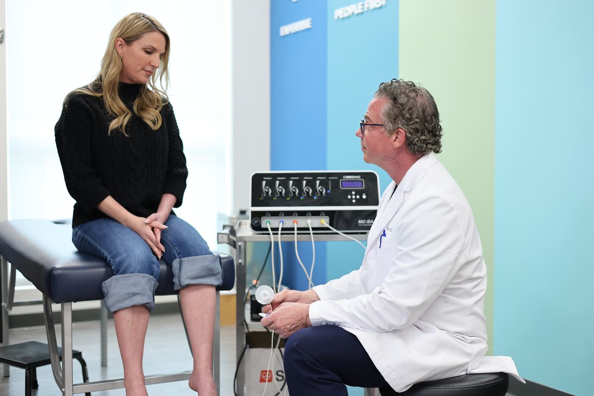 Dr. Barton talking with a patient in the scrambler therapy room, the machine beside them.