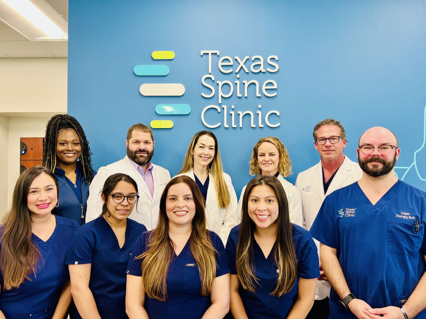 The Texas Spine Clinic team in front of the clinic's logo wall.