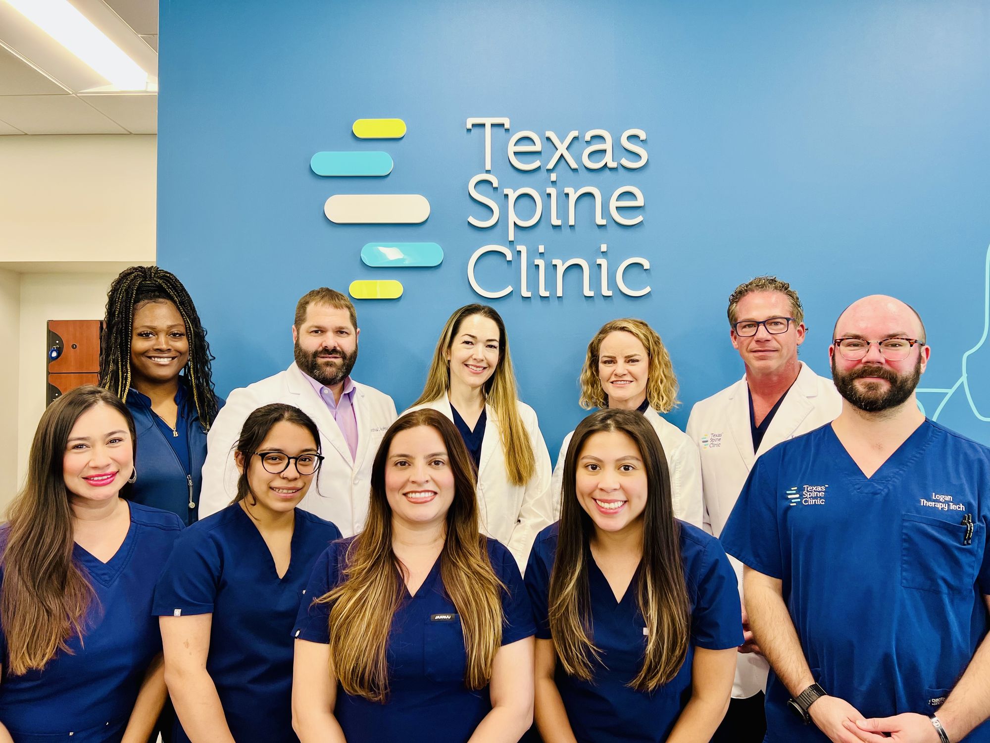 The Texas Spine Clinic team in front of the clinic's logo wall.