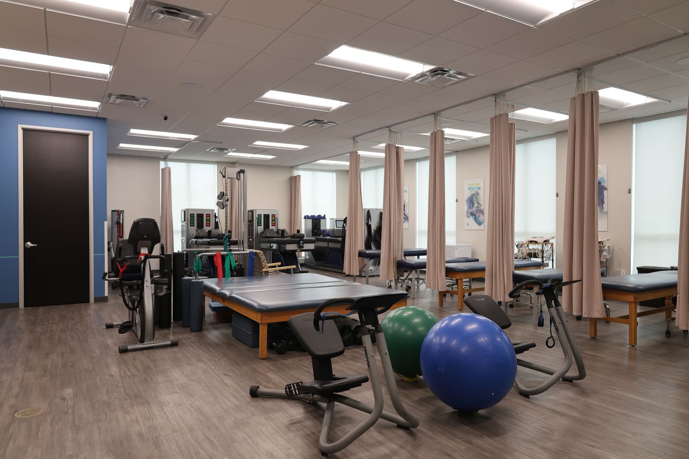 The therapy room at Texas Spine Clinic: curtained treatment bays, therapy tables, exercise bikes and stability balls.