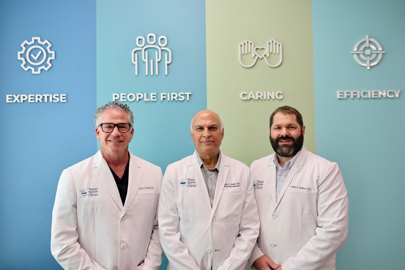 Kevin S. Barton, D.C., Praful C. Singh, M.D., and Joshua C. Huffman, D.C., at the Texas Spine Clinic values wall.
